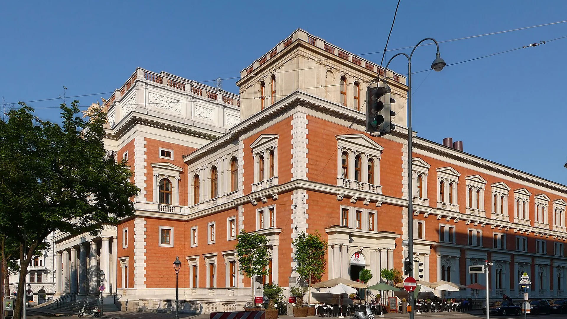 The Börse palace on Vienna's Ringstraße from the corner, a brick-red building with white stone window frames, a balustraded roofline and a tall corner block against a blue sky.