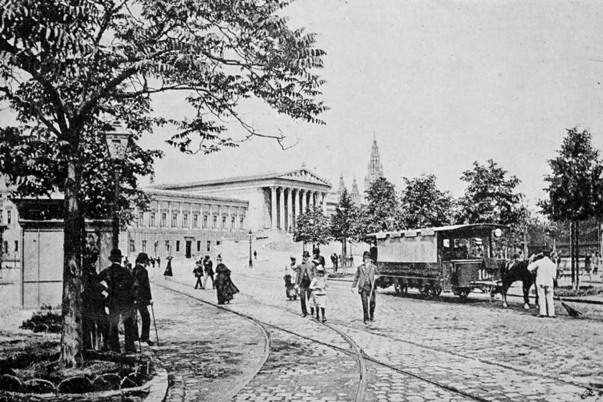 A black-and-white photograph of the Ringstraße in 1890, with the Parliament building behind a horse tram and strolling pedestrians